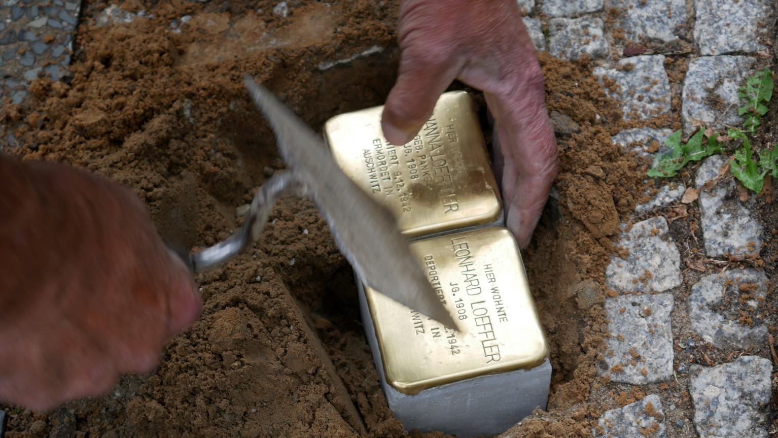 Stolpersteinverlegung, zwei Stolpersteine werden zwischen Pflastersteine gesetzt